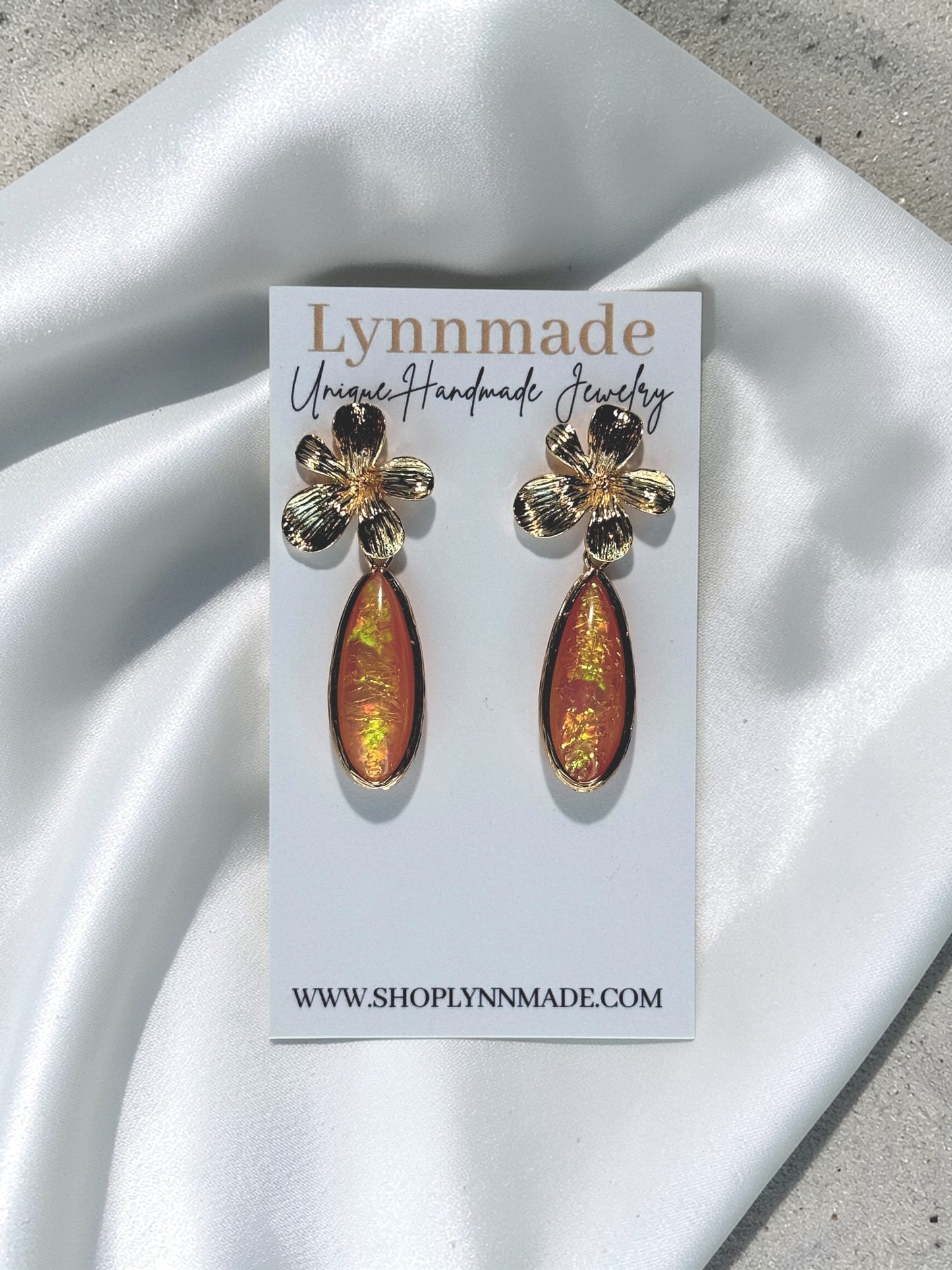 A pair of Lynnmade handmade earrings featuring gold-toned hibiscus flower studs with iridescent orange coral teardrop charms