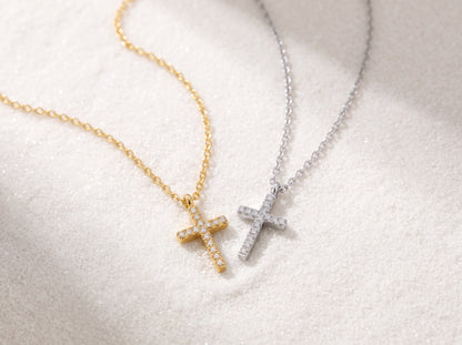 A close-up view of a dainty 14k gold-plated tiny cross necklace, featuring a delicate yellow gold chain and a petite cross pendant closely set with sparkling cubic zirconia (CZ) diamonds, shown as a fine jewelry product display and worn on a model.