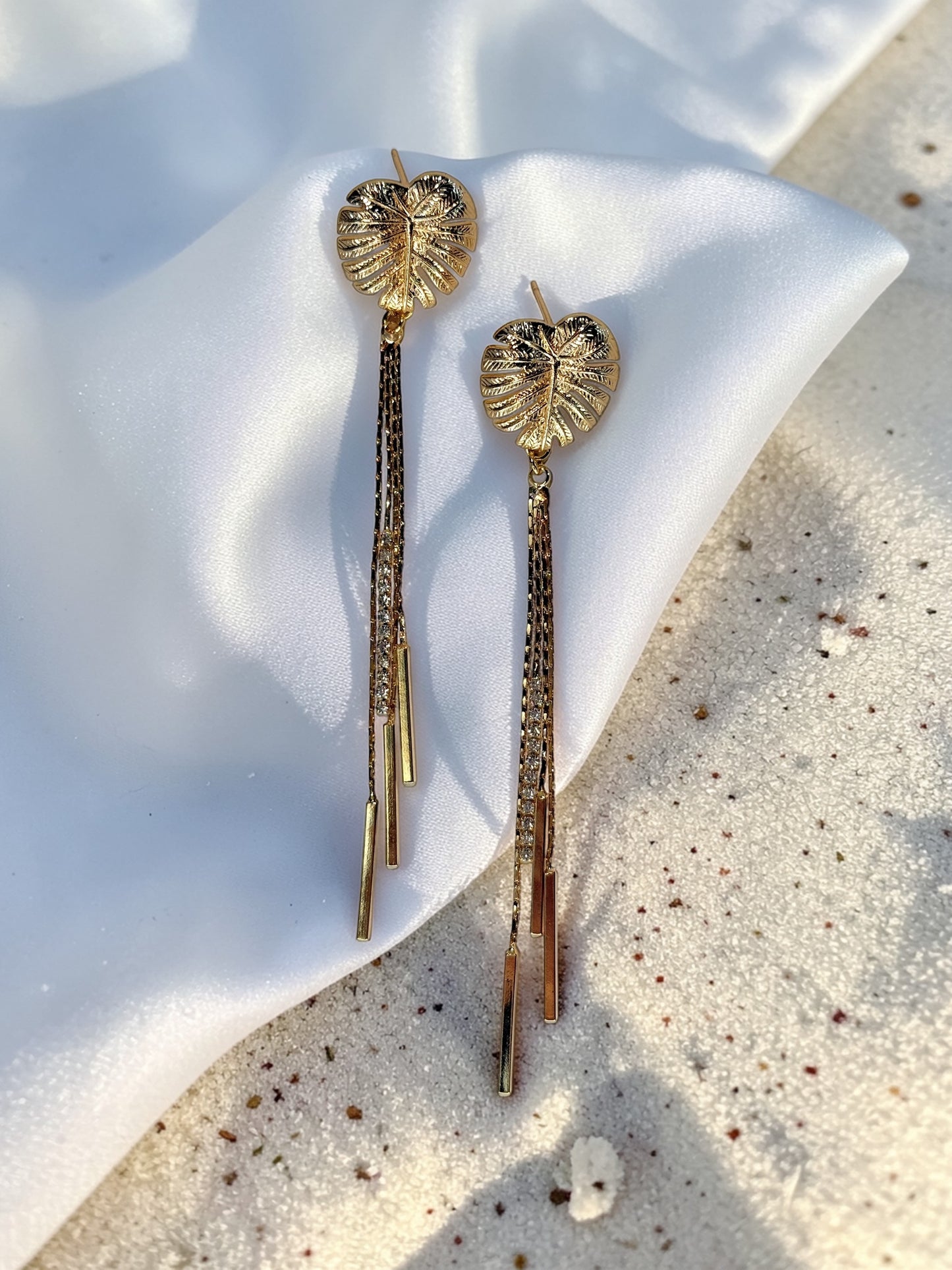 Pair of gold Long Monstera Tassel Earrings with textured leaf studs and shimmering chain fringe.