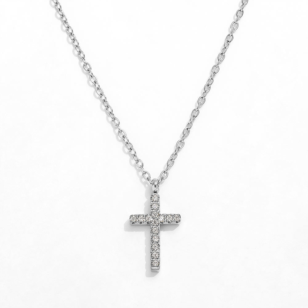 A close-up view of a dainty 14k gold-plated tiny cross necklace, featuring a delicate yellow gold chain and a petite cross pendant closely set with sparkling cubic zirconia (CZ) diamonds, shown as a fine jewelry product display and worn on a model.