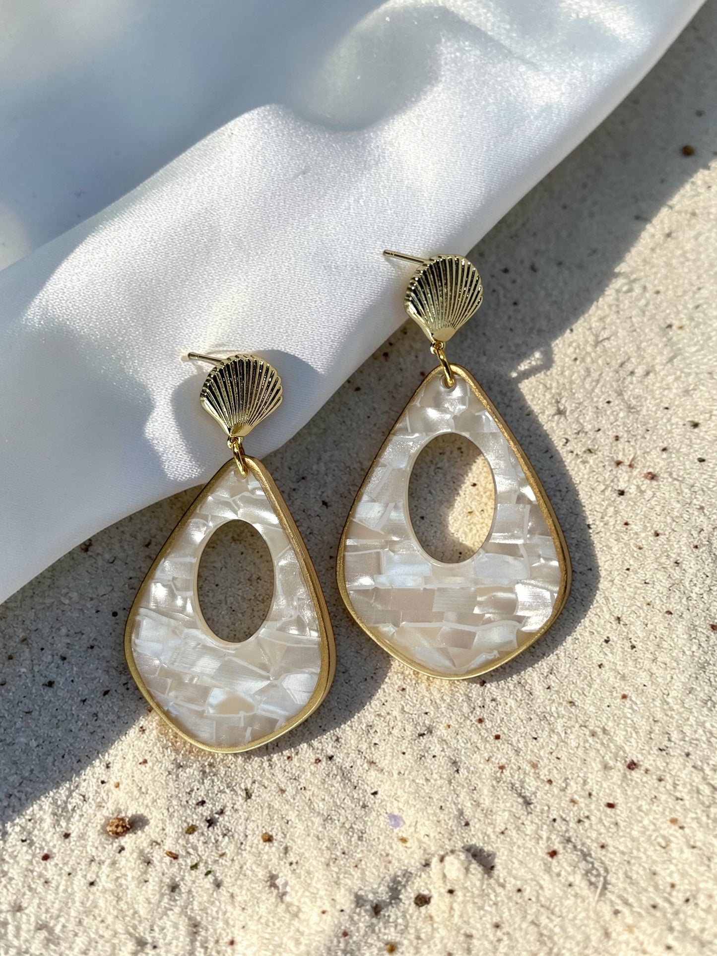 Luminous Tide Mother of Pearl Shell Drop Earrings in Gold or Silver on white silk and sand background.