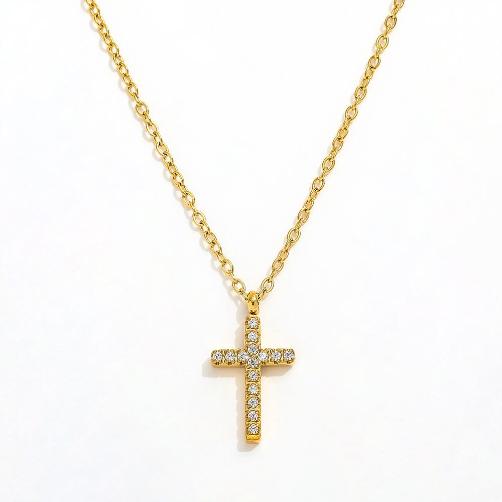 A close-up view of a dainty 14k gold-plated tiny cross necklace, featuring a delicate yellow gold chain and a petite cross pendant closely set with sparkling cubic zirconia (CZ) diamonds, shown as a fine jewelry product display and worn on a model.